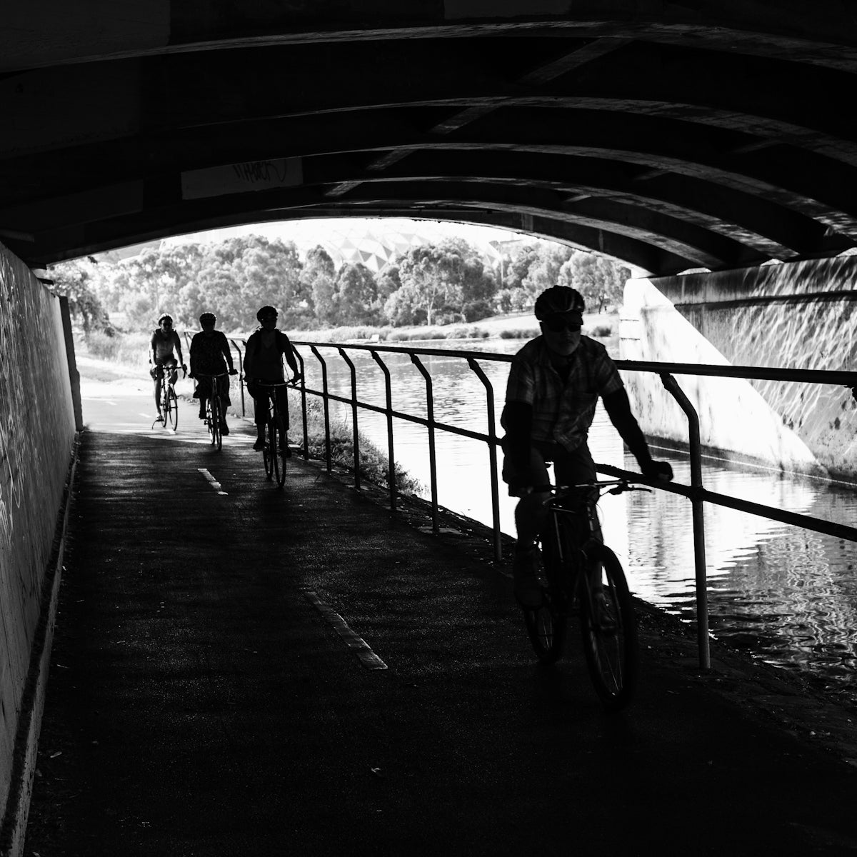 a black and white photo of people riding bikes under a bridge