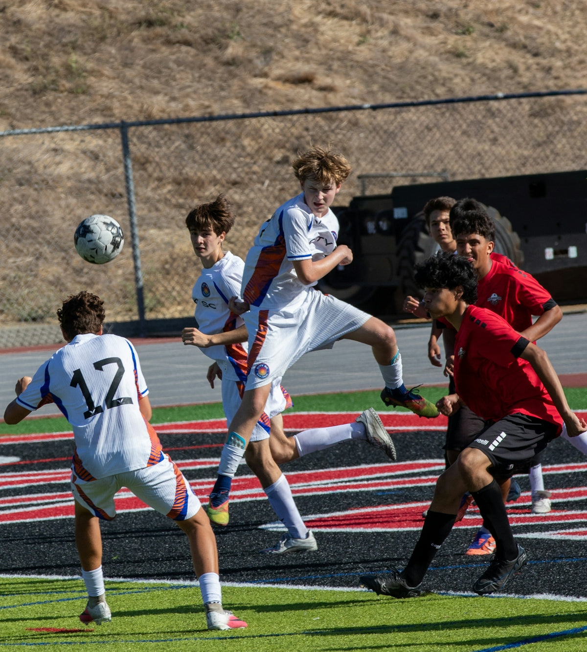 Teenage boys playing soccer, one jumping for a header.